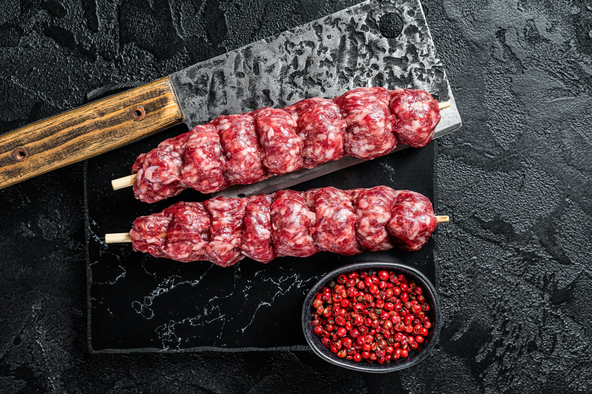 Raw beef Kofta kebab Skewers on a meat cleaver. Black background. Top view